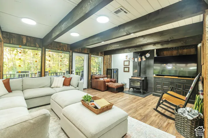 Exposed dark-finish ceiling beams, wood-finish flooring, floor-to-ceiling windows, built-in cabinetry, and a freestanding wood-burning stove with stone surround