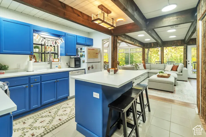 Kitchen featuring a central island with a solid surface countertop, blue cabinetry, exposed wooden ceiling beams, and a geometric pendant light fixture