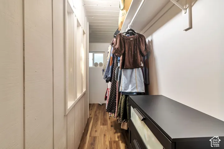 Storage area featuring wood-finish flooring, vertical panel wall detailing, and fixed shelving
