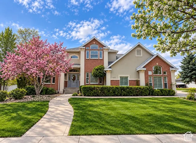 Two-story traditional exterior featuring brick and stucco siding, arched multi-pane windows, a covered entryway with stone steps, and a concrete walkway
