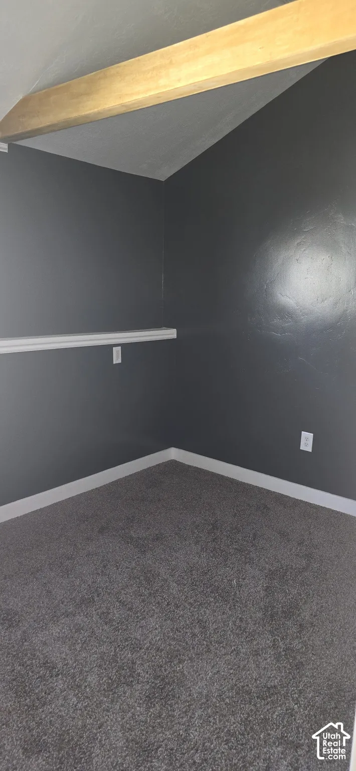Interior space featuring a vaulted ceiling with an exposed wood beam, wall-to-wall carpeting, and a chair rail
