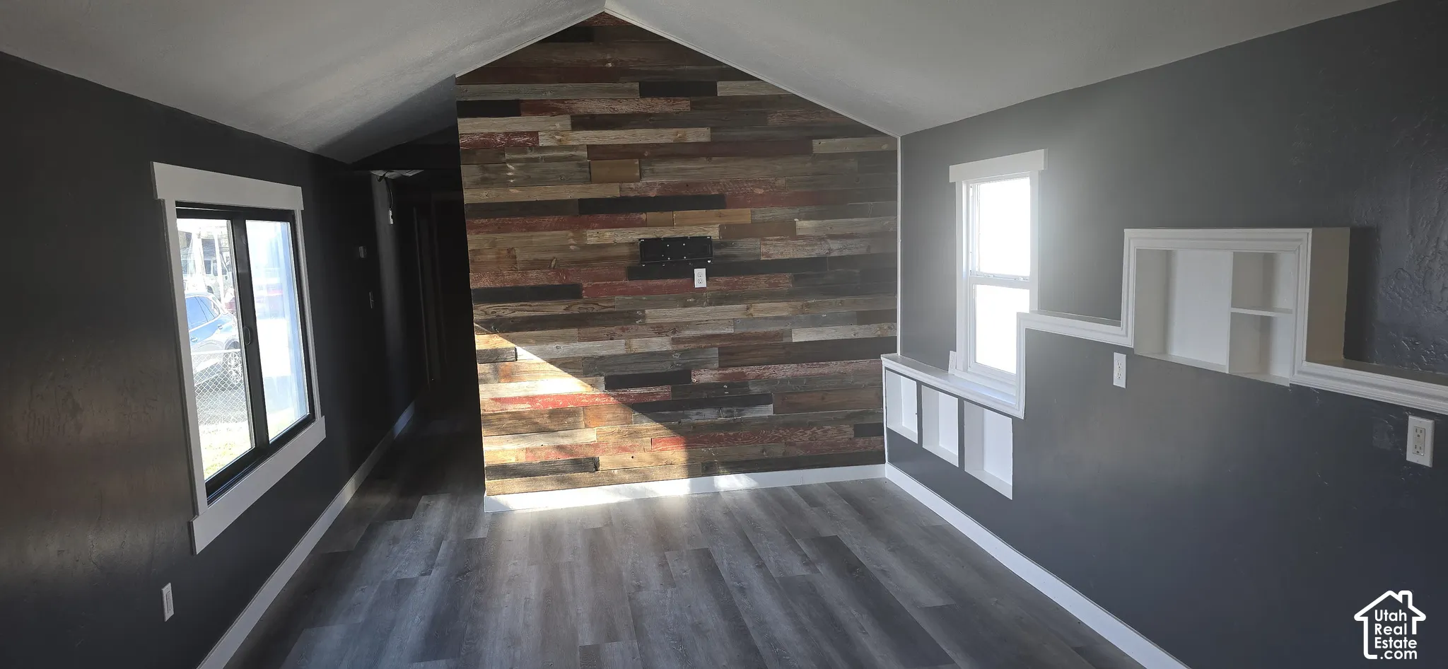 Vaulted ceiling interior featuring wood-finish flooring, a decorative wood-plank accent wall, and built-in recessed shelving