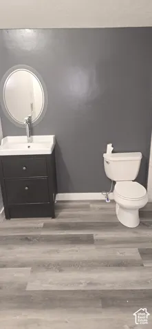 Dark-toned vanity with integrated basin, polished metal faucet, oval wall-mounted mirror, two-piece porcelain toilet, and wood-finish flooring