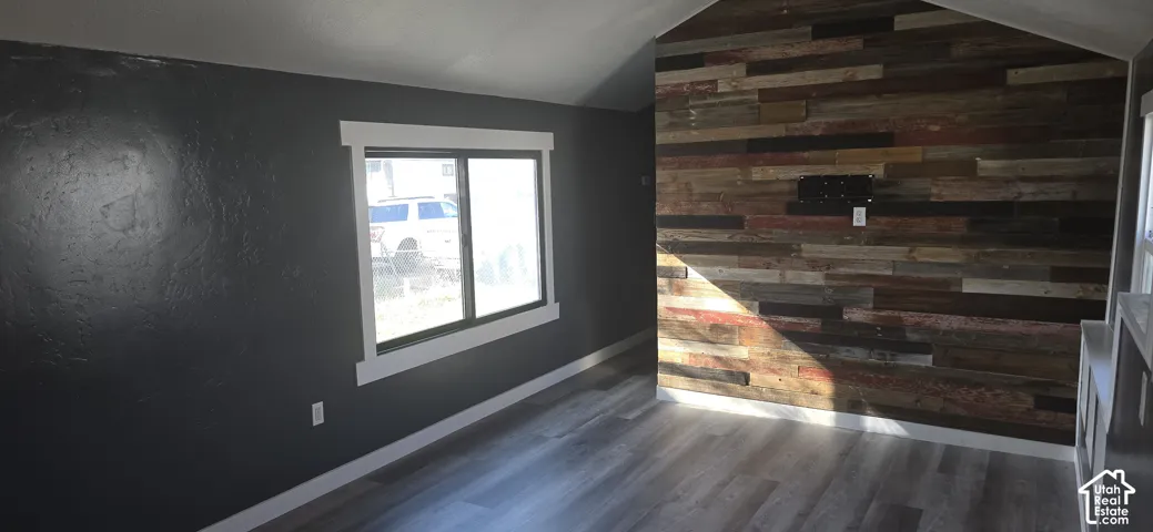 Vaulted ceiling featuring a reclaimed wood accent wall, wood-finish flooring, dark-toned walls, and thick white window trim