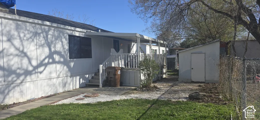 Exterior featuring white vertical siding, a covered deck with railings, a detached storage shed, and chain-link perimeter fencing