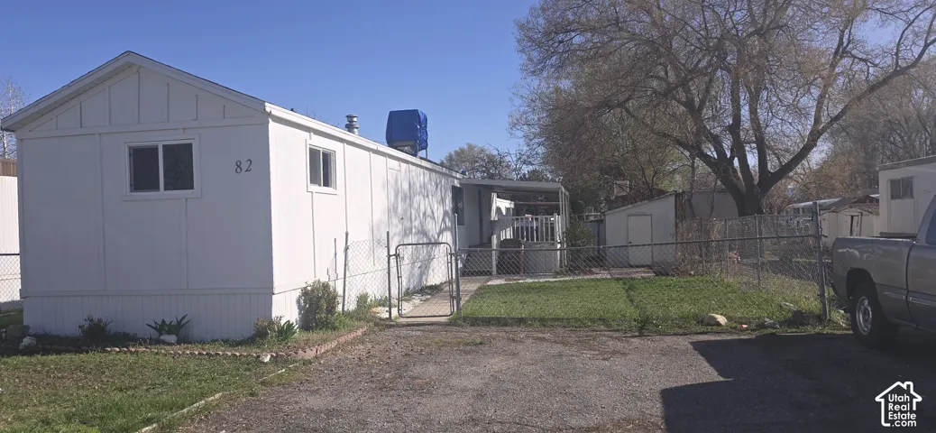 Exterior featuring white siding, a metal chain-link perimeter fence with gate, a paved driveway, and a detached storage structure