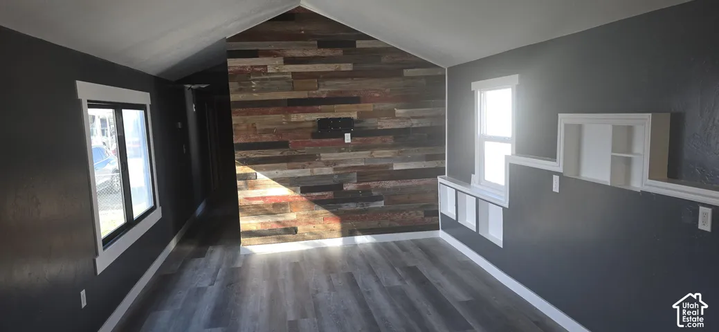 Vaulted ceiling interior featuring wood-finish flooring, a decorative wood-plank accent wall, and built-in recessed shelving