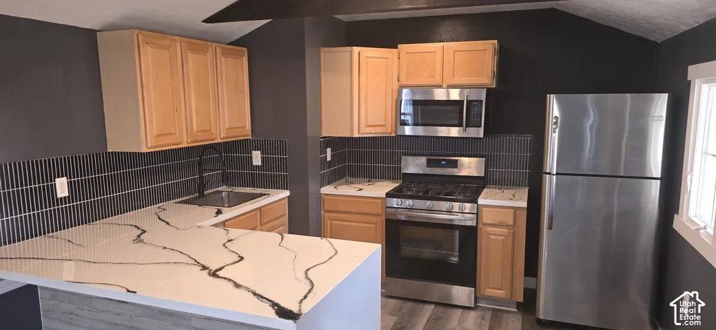 Kitchen featuring light-finish cabinetry, patterned countertops, stainless steel appliances, vertical tile backsplash, and dark-finish plumbing fixtures
