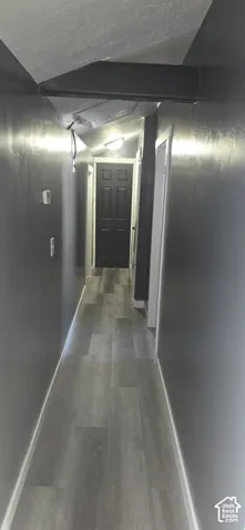 Hallway featuring wood-finish flooring, charcoal-toned walls, a dark-finished interior door with a six-panel design, and a ceiling-mounted light fixture