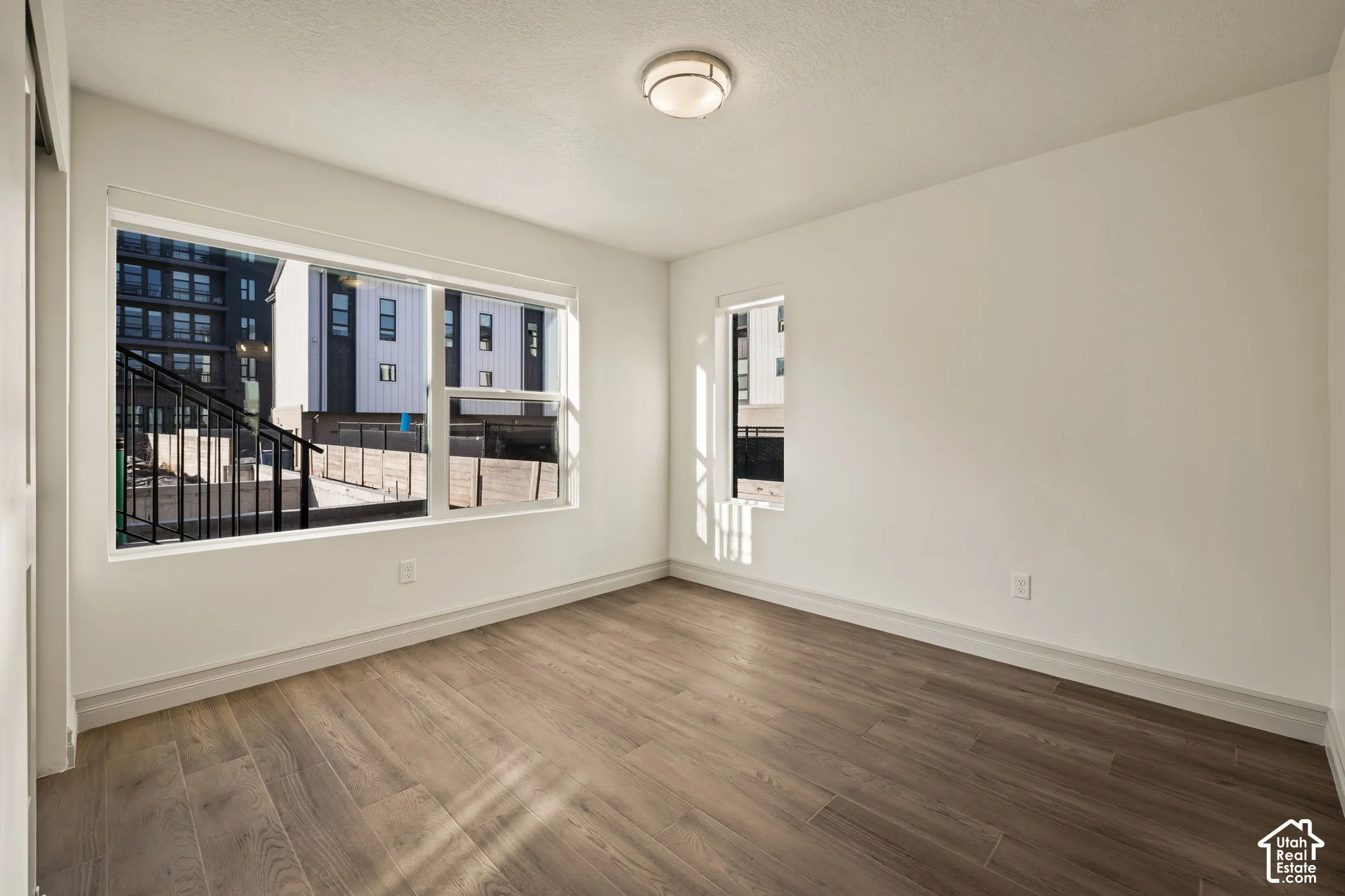 Wood-finish flooring, neutral walls, large windows, and a flush-mount ceiling light fixture