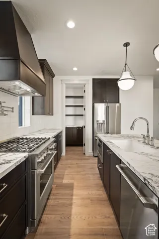 Kitchen featuring dark cabinetry, stone countertops, stainless steel professional-grade range, wall-mounted pot filler, and wood-finish flooring