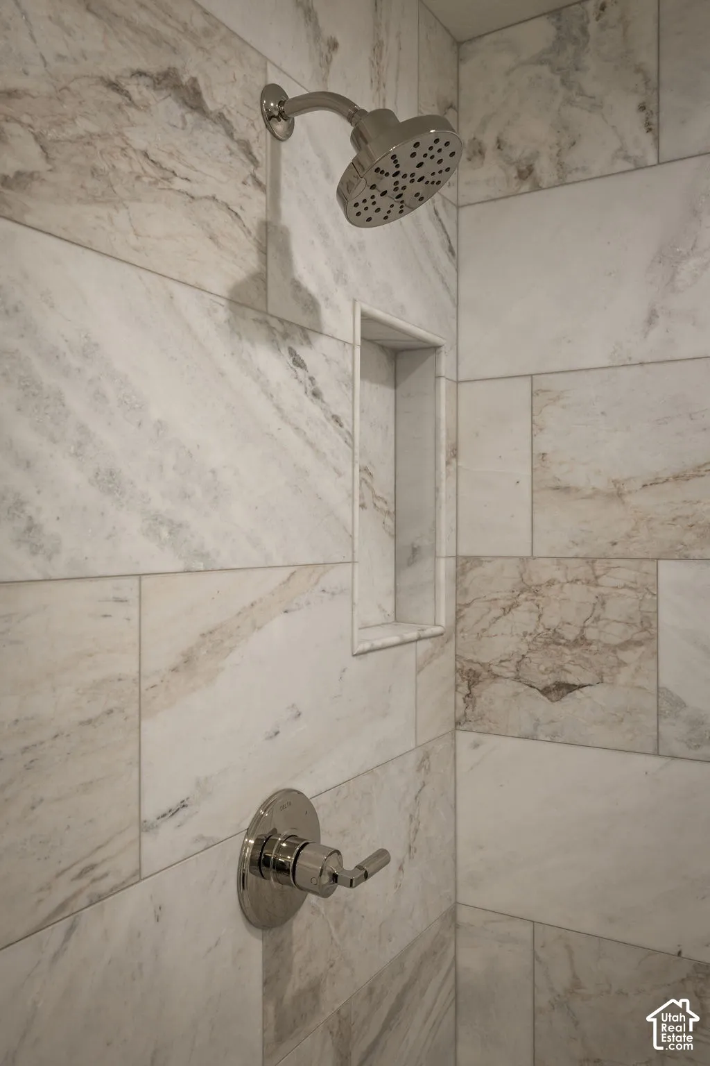 Shower stall featuring large-format stone-tile surround, integrated recessed shelving, polished chrome showerhead, and matching single-handle pressure-balance valve