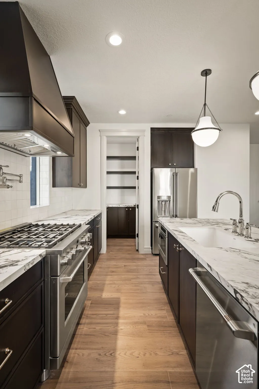 Kitchen featuring dark cabinetry, stone countertops, stainless steel professional-grade range, wall-mounted pot filler, and wood-finish flooring