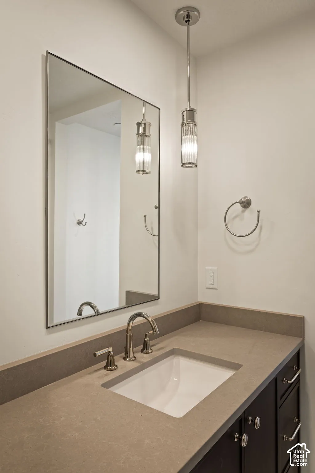 Vanity featuring a solid-surface countertop, integrated rectangular undermount sink, polished metal widespread faucet, fluted glass pendant lighting, and framed mirror