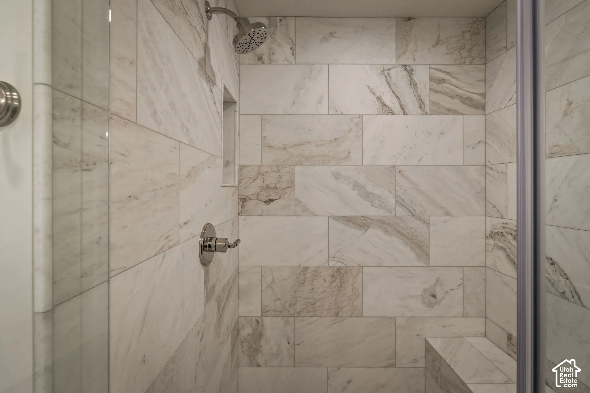 Shower stall featuring floor-to-ceiling stone-pattern tile, built-in recessed wall niche, tiled corner bench, and polished chrome fixtures