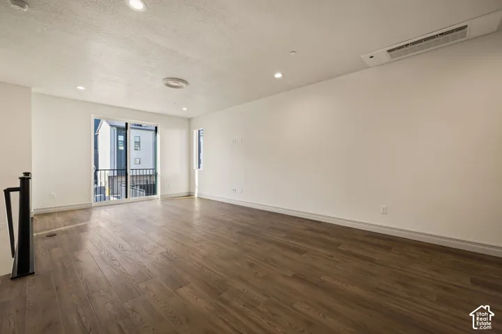 Open-concept interior featuring wood-finish flooring, recessed lighting, and a glass sliding door leading to an exterior balcony with black metal railing