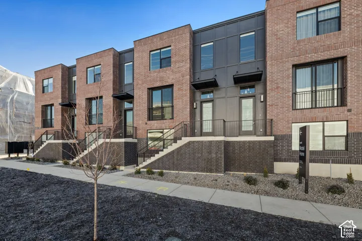 Multi-story exterior featuring a mix of red and dark masonry, vertical metal paneling, large rectangular windows, and metal stair railings