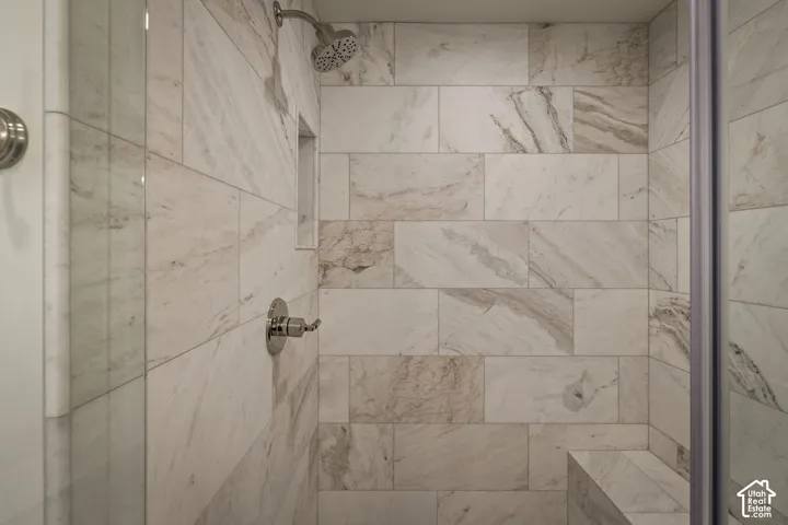 Shower stall featuring floor-to-ceiling stone-pattern tile, built-in recessed wall niche, tiled corner bench, and polished chrome fixtures