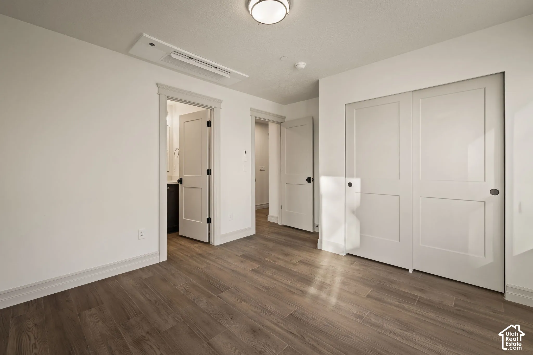 Room interior featuring wood-finish flooring, two-panel interior doors with matte black hardware, and double sliding closet doors