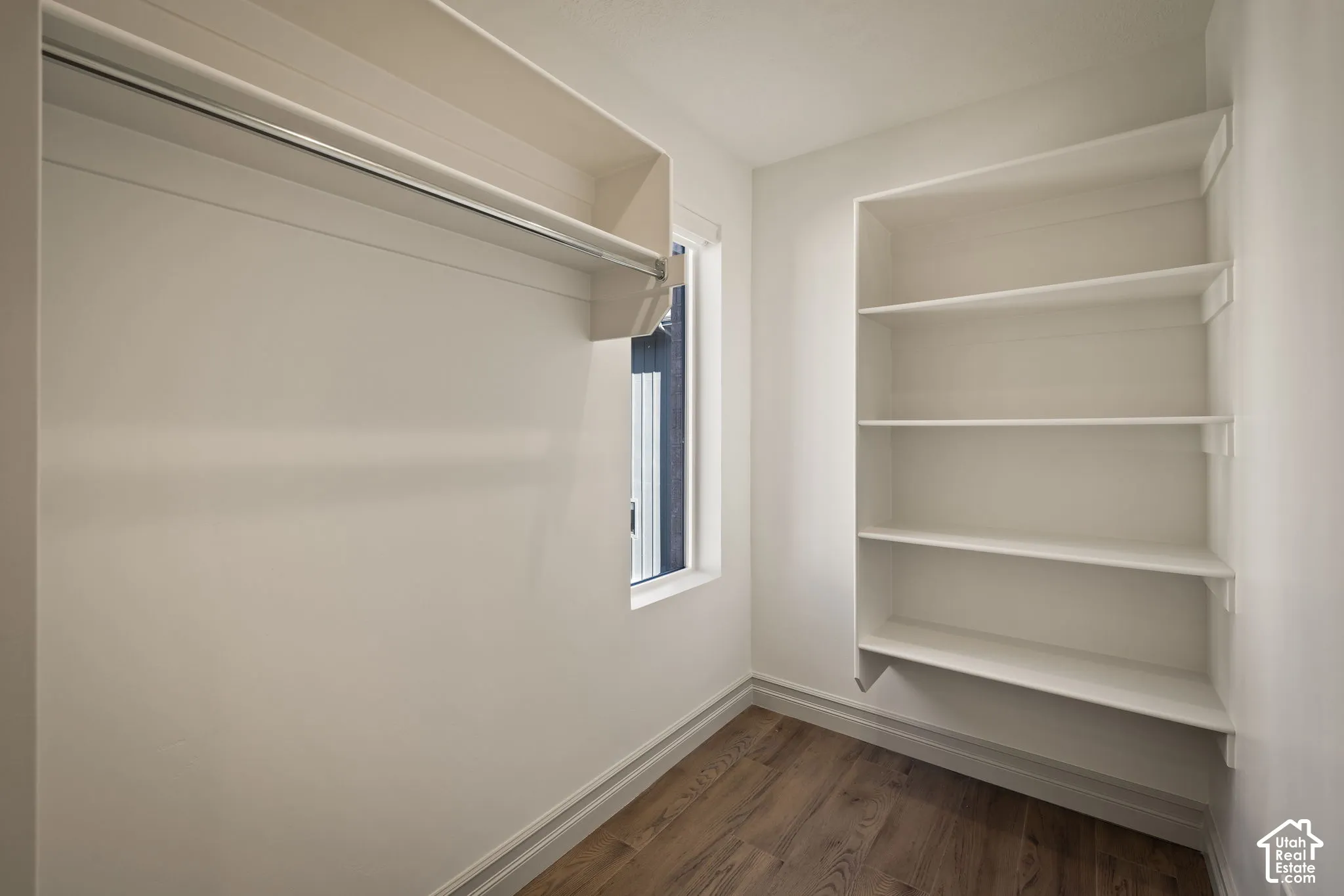 Walk-in closet featuring wood-finish flooring, built-in shelving, a dedicated clothing rod, and a window for natural light