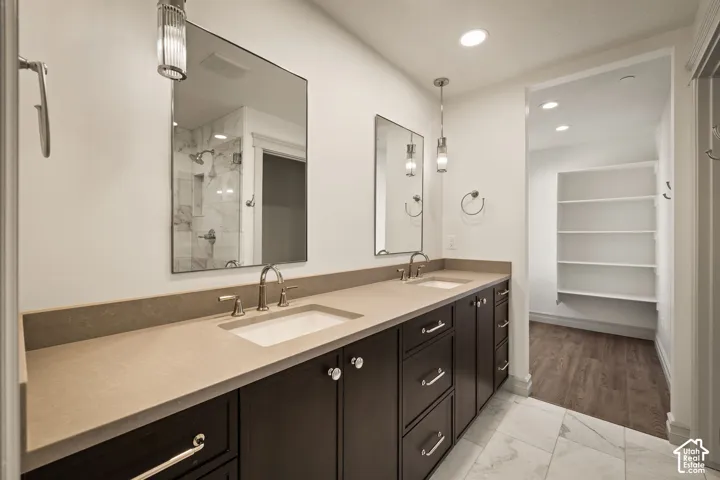 Dual-sink vanity with dark cabinetry and solid-surface countertop, tile flooring, wall-mounted light fixtures, and built-in shelving