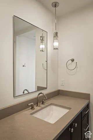 Vanity featuring a solid-surface countertop, integrated rectangular undermount sink, polished metal widespread faucet, fluted glass pendant lighting, and framed mirror