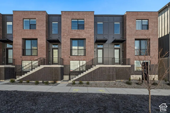 Multi-story exterior featuring a red and dark-toned brick facade, industrial-style metal paneling, large rectangular windows, and elevated entryways with metal railings
