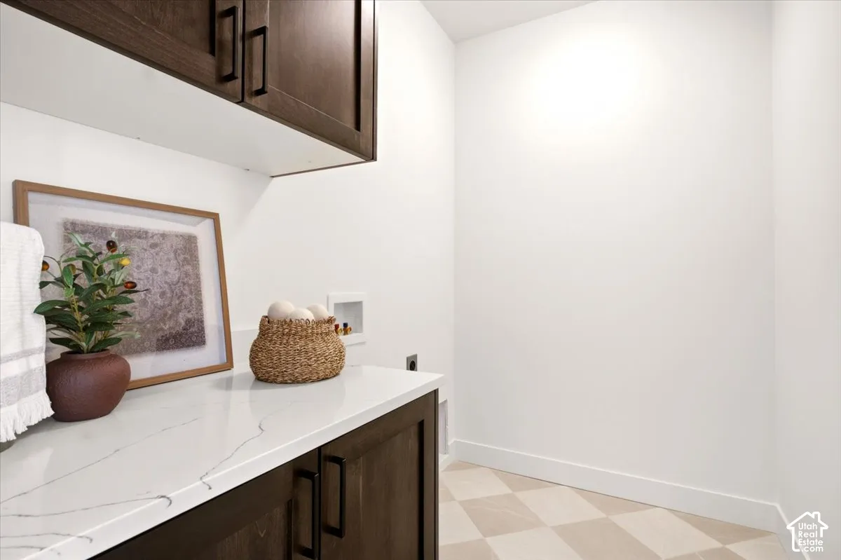 Utility room featuring dark-stained wood cabinetry, white stone-finish countertop, and tile flooring with a checkerboard pattern