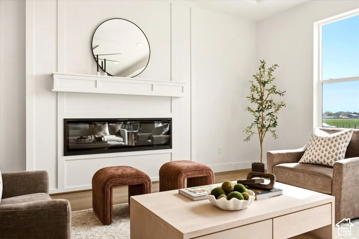 Linear fireplace featuring a minimalist mantel and decorative millwork paneling, complemented by wood-finish flooring and a tall window