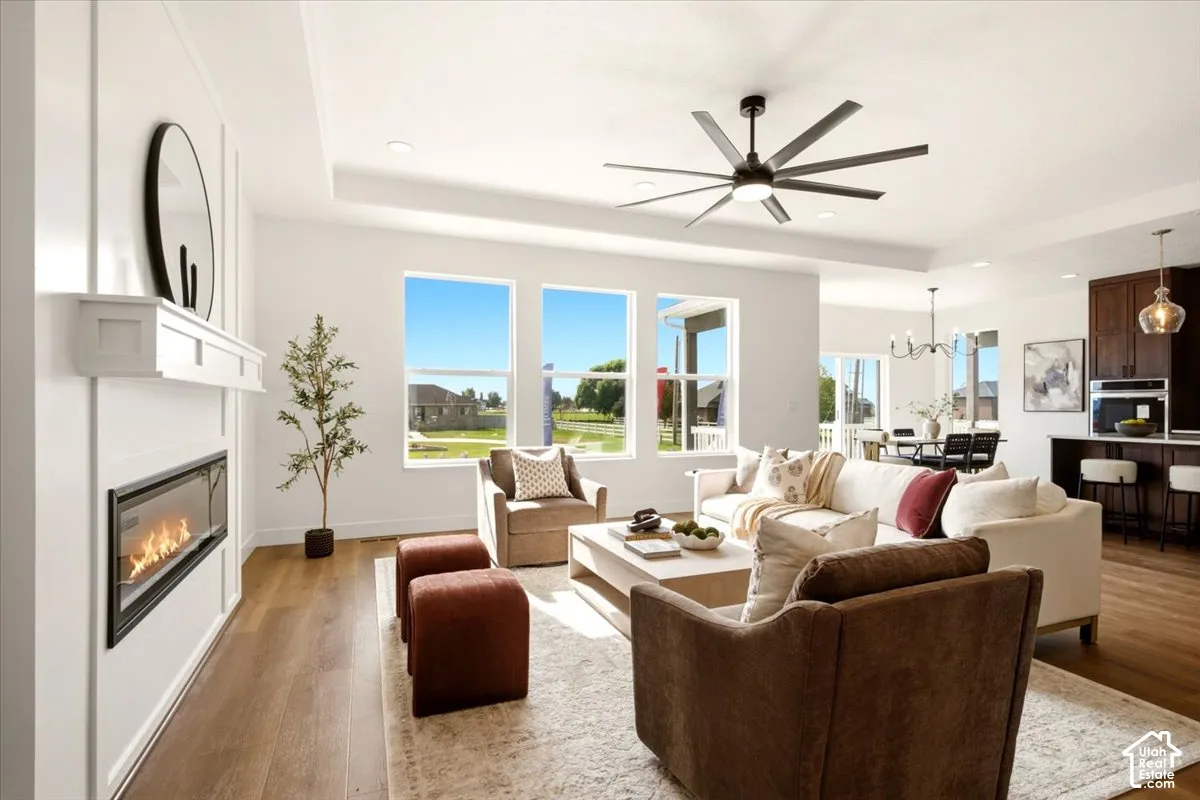 Living space featuring a tray ceiling, recessed lighting, multi-blade ceiling fan, linear fireplace with a white mantel, and wood-finish flooring