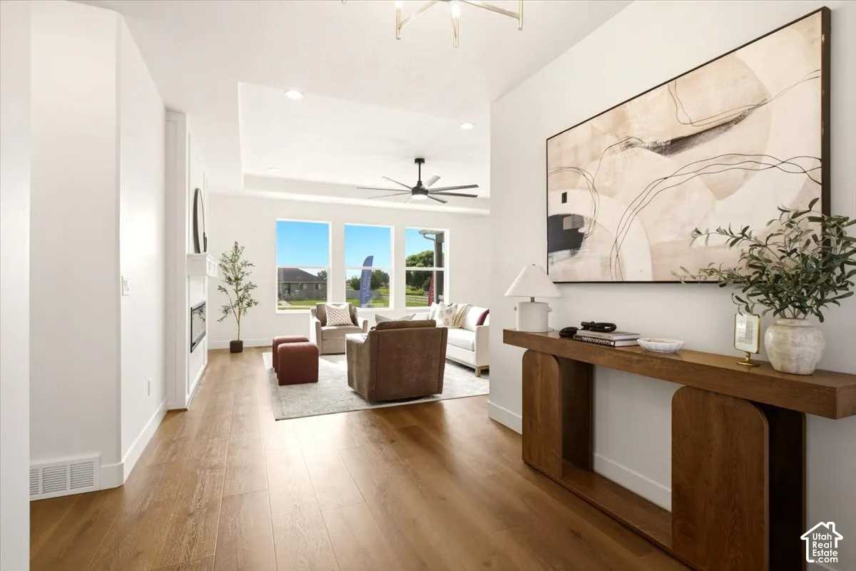 Living area featuring wood-finish flooring, a recessed tray ceiling, a sleek ceiling fan, and large windows
