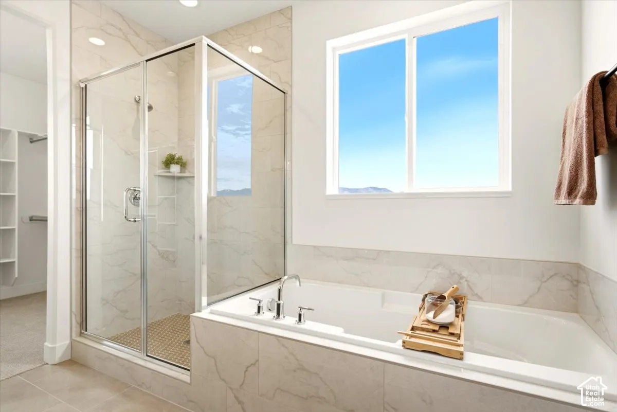 Walk-in shower with a glass enclosure, porcelain tile surround, built-in shelving, deep soaking tub, and tile deck
