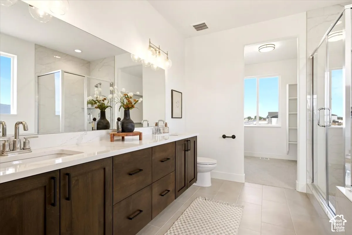 Dark wood-finish cabinetry, white countertop with dual under-mount sinks, oversized wall-to-wall mirror, glass-enclosed shower, and tile flooring