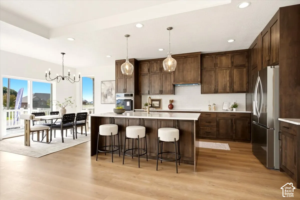 Kitchen featuring custom wood cabinetry, a central island with a light-toned countertop, wood-finish flooring, subway tile backsplash, and recessed lighting