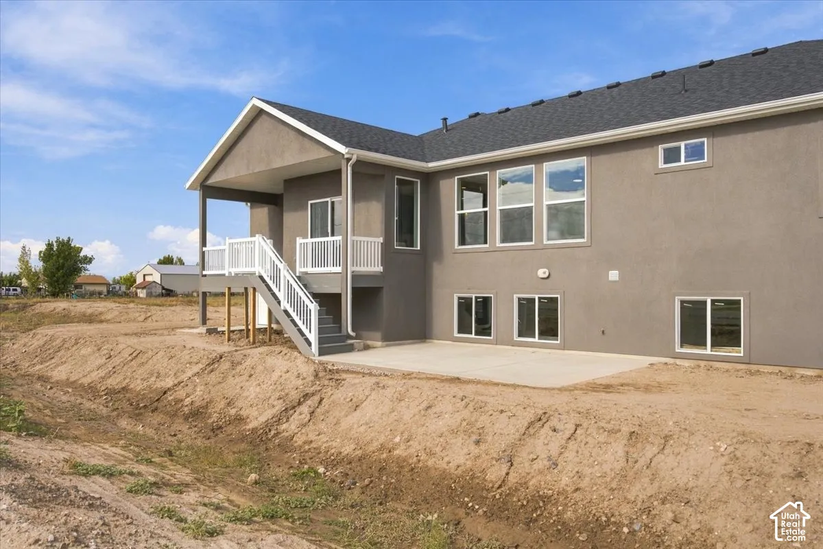 Stucco exterior featuring a raised covered deck with white railing, a concrete ground-level patio, and multiple rectangular windows