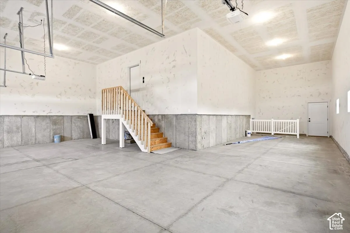 Spacious garage featuring concrete flooring, textured ceiling, concrete perimeter walls, and an integrated staircase with wooden railings