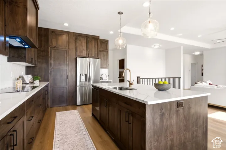 Kitchen featuring dark wood cabinetry, a central island with a solid surface countertop, stainless steel appliances, pendant lighting, and wood-finish flooring