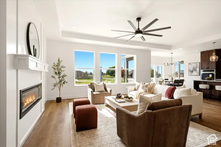 Living space featuring a tray ceiling, recessed lighting, multi-blade ceiling fan, linear fireplace with a white mantel, and wood-finish flooring