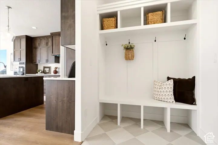 Built-in white mudroom bench featuring integrated cubbies and wall-mounted hooks, offset by wood-finish flooring and dark-toned cabinetry in the surrounding area
