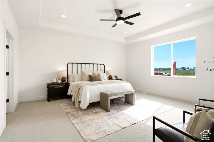 Spacious room featuring a tray ceiling, neutral carpet flooring, recessed lighting, and a multi-blade ceiling fan