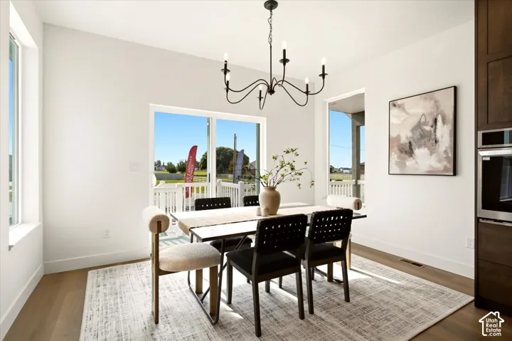 Dining area featuring wood-finish flooring, a contemporary six-arm chandelier, large windows, and a sliding glass door
