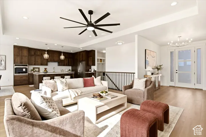 Open concept floor plan featuring a multi-blade ceiling fan, recessed lighting, wood-finish flooring, dark wood-tone cabinetry, and a tiered tray ceiling