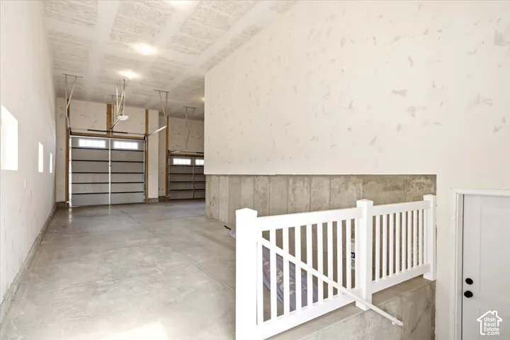 Multi-car garage featuring high ceilings with integrated lighting, textured wall finishes, dual overhead garage doors, concrete flooring, and a white railing enclosure