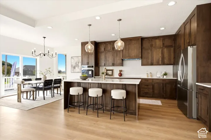Kitchen featuring custom wood cabinetry, a central island with a light-toned countertop, wood-finish flooring, subway tile backsplash, and recessed lighting