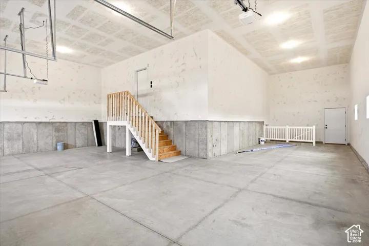 Spacious garage featuring concrete flooring, textured ceiling, concrete perimeter walls, and an integrated staircase with wooden railings