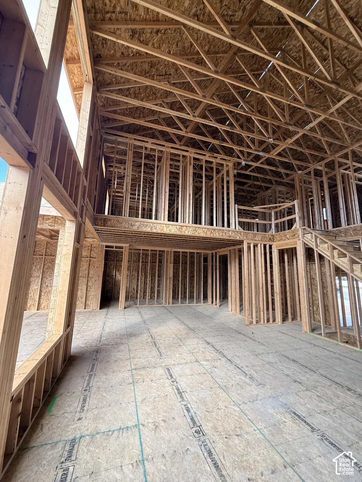 New construction framing featuring an open-concept interior, exposed engineered roof trusses, two-story ceiling height, and structured wooden stair framing
