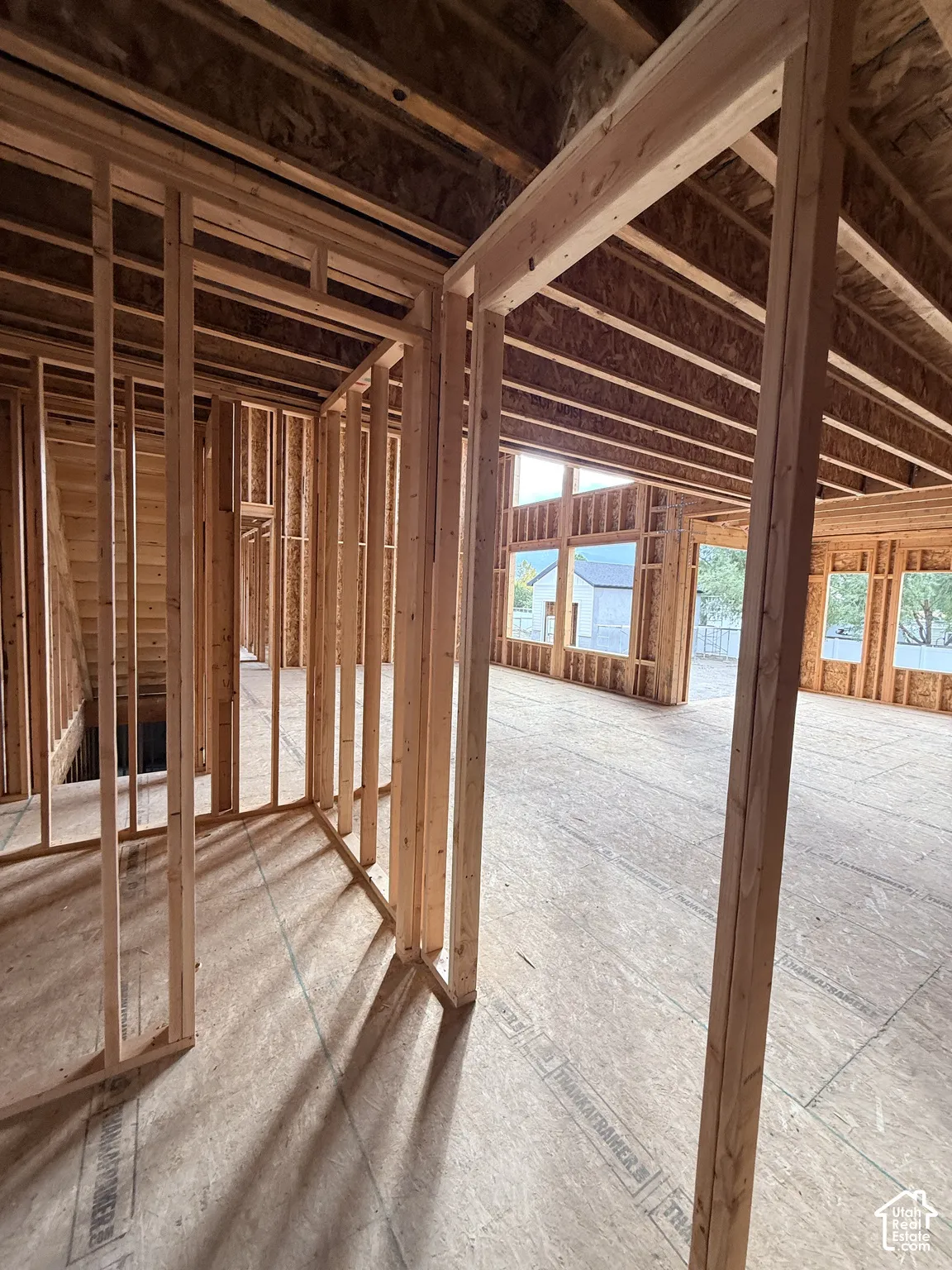 New construction framing featuring exposed wall studs, subfloor decking, timber ceiling joists, and multiple window openings