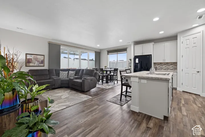Open-concept floor plan featuring wood-finish flooring, recessed lighting, a kitchen island with stone-finish countertops, and white cabinetry