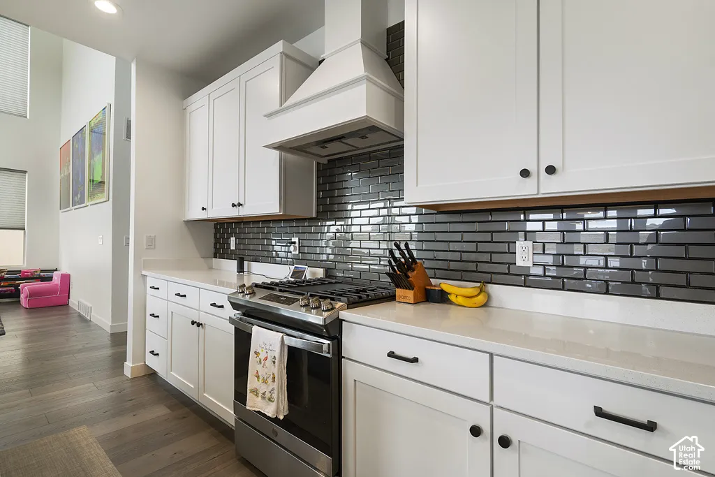 Kitchen featuring white shaker-style cabinetry, a glossy dark tile backsplash, quartz countertops, a matching range hood, and stainless steel gas range