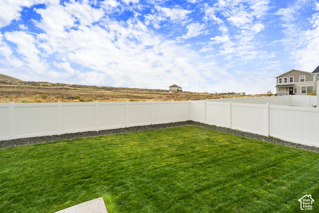 Fenced backyard featuring a manicured lawn, stone aggregate border, and mountain horizon